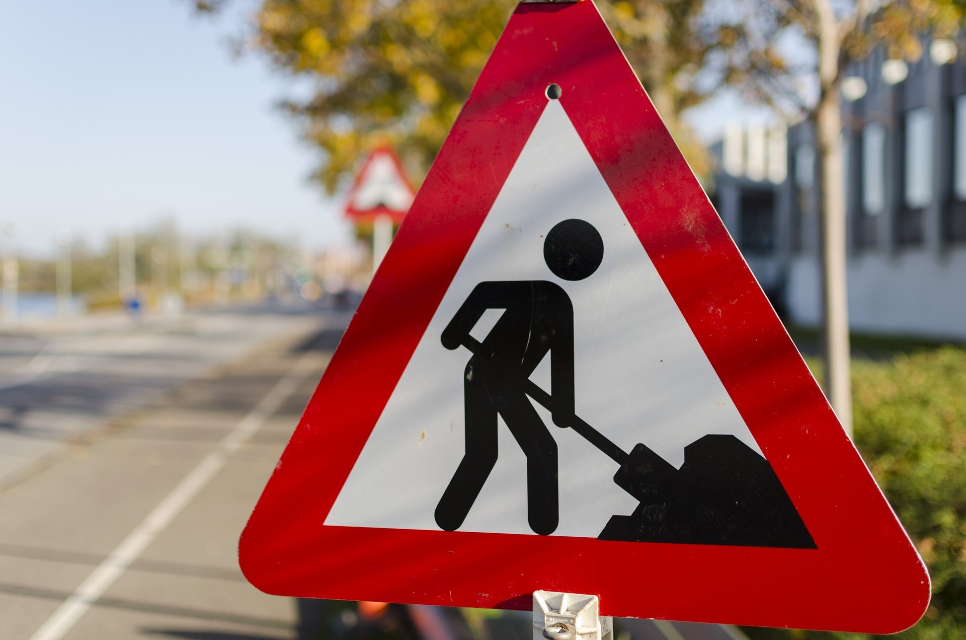 Weißes dreieckiges Schild mit roter Umrandung auf dem in schwarz ein Mensch mit einer Schippe und einem Haufen dargestellt ist. 