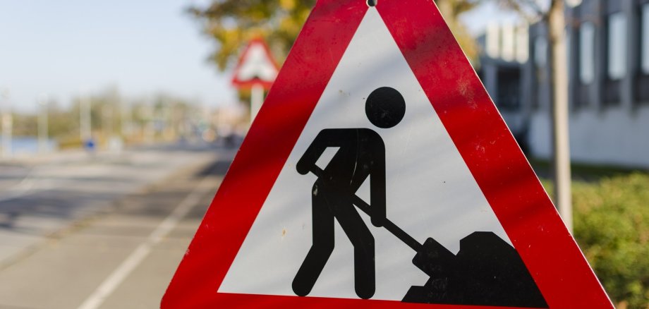Weißes dreieckiges Schild mit roter Umrandung auf dem in schwarz ein Mensch mit einer Schippe und einem Haufen dargestellt ist. 