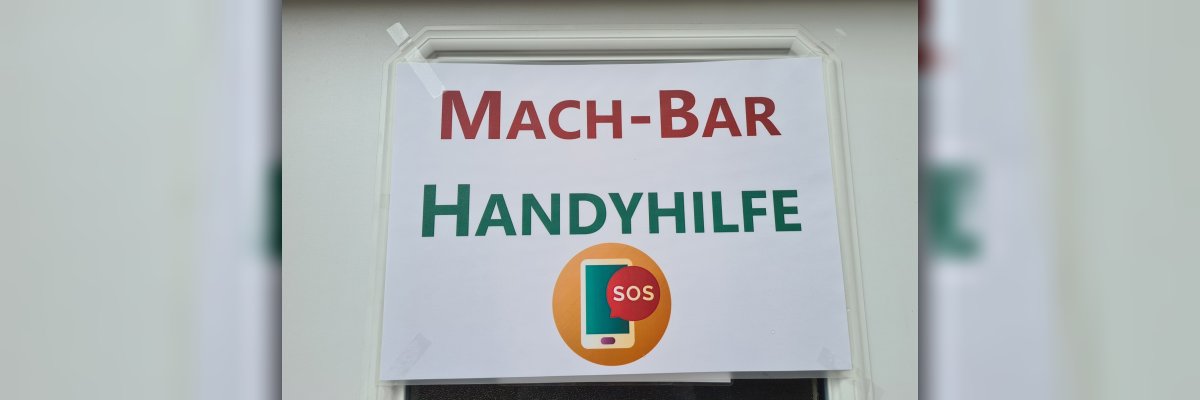 Handyhilfe Hier hängt ein Schild an einer Tür. Auf dem Schild steht "Mach-Bar Handhilfe". Darunter ist ein Handy abgebildet mit einer SOS-Sprechblase.