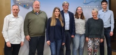 Bild der Mitglieder des Arbeitskreises Digitales und dem Referenten Jürgen Reincke. Von links nach rechts: Herr Rapp, Herr Reincke, Frau Marotte, Herr Hirsch, Frau Rimlinger, Frau Odenwald und Herr Decker. Im Hintergrund sieht man das Verbandsgemeindelogo.