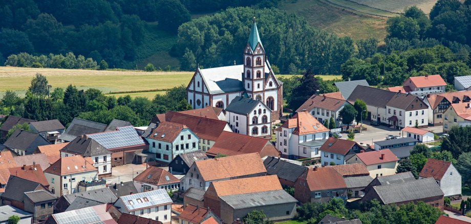 Martinshöhe Kirche umgeben von Häusern hinter der ein Feld liegt.