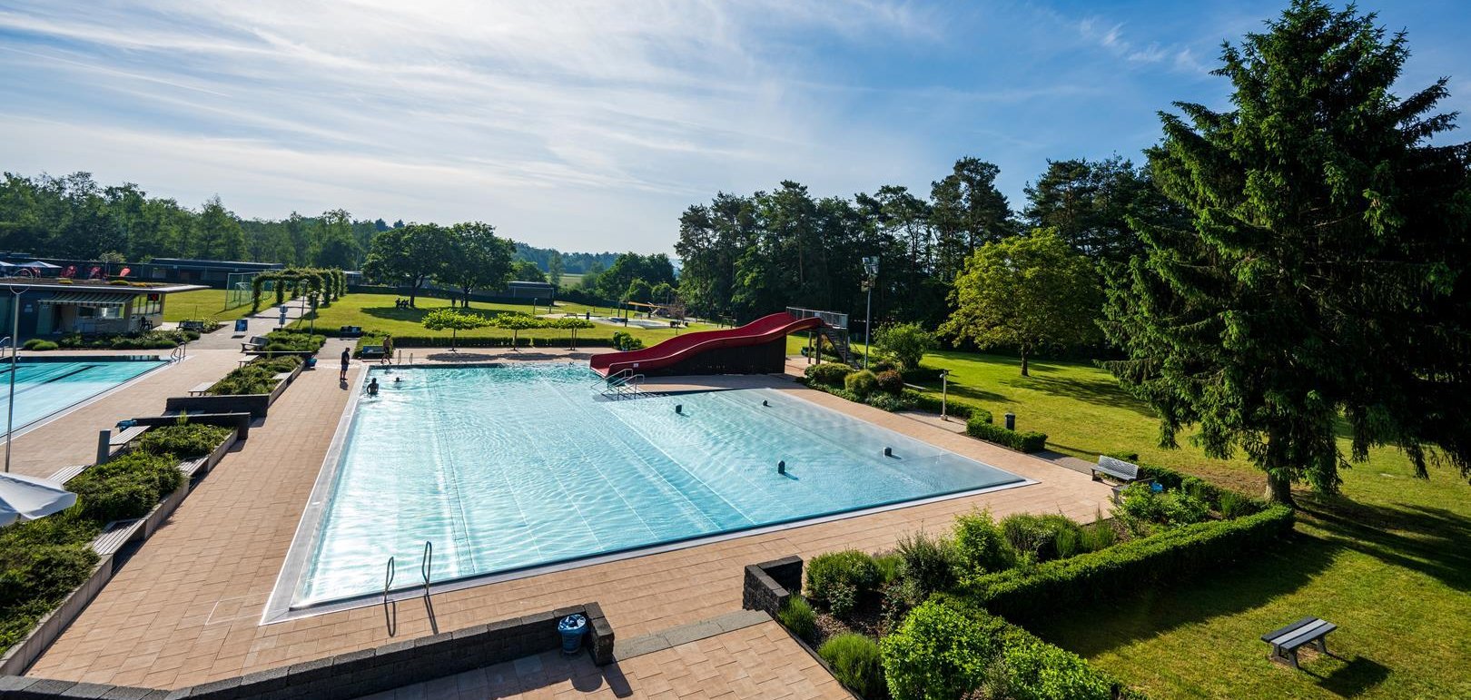 Schwimmbecken mit roter Rutsche und Liegewiese.