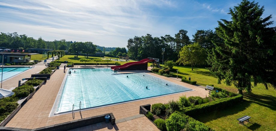 Freibad von oben Schwimmbecken mit roter Rutsche und Liegewiese.