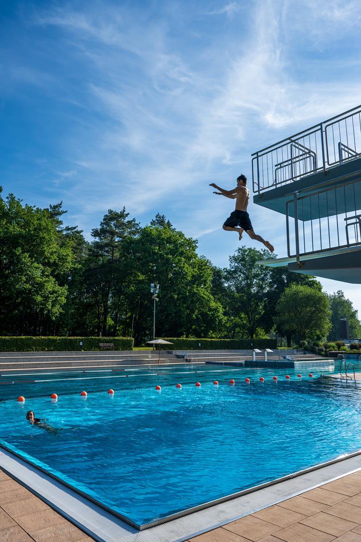 Junge der vom Sprungturm ins Schwimmbecken springt.