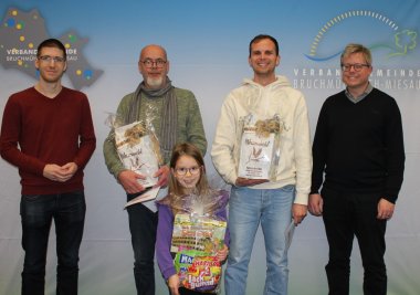 2024 fand ein Digitales Weihnachtsquiz statt. Dazu  gab es eine Preisverleihung für die Gewinner. Von links nach rechts: Herr Decker, die drei Gewinner und Herr Hirsch. Vor der Fotowand der Verbandsgemeinde.